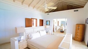 Een slaapkamer met een groot bed, een nachtkastje, een dressoir, een plafondventilator en een zichtbare badkamer door een open deur.