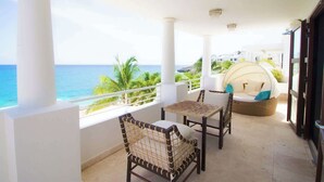 Een balkon met wickerstoelen en een zitzonetje met kussens, met uitzicht op de oceaan.