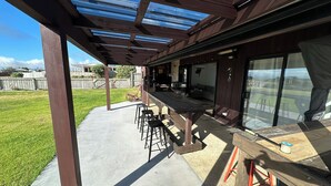 An outdoor patio with a wooden table and chairs, a covered seating area, and a view of the backyard.