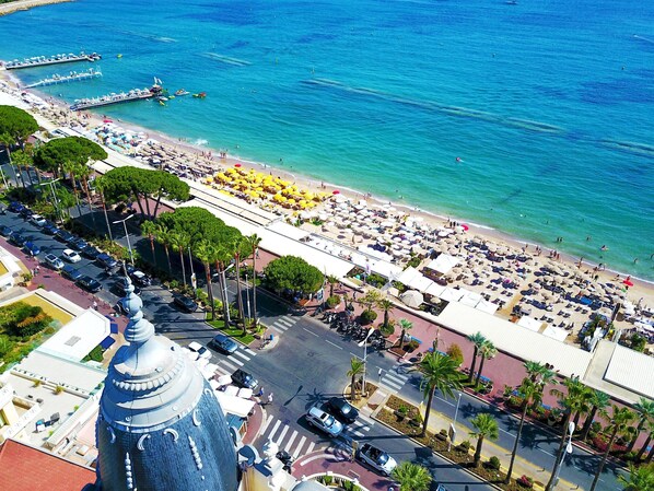 A coastal cityscape with a prominent tower, a busy beach with umbrellas, and a marina.