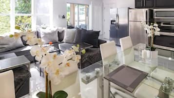 A modern kitchen with stainless steel appliances, a glass dining table, and a sofa with decorative pillows.