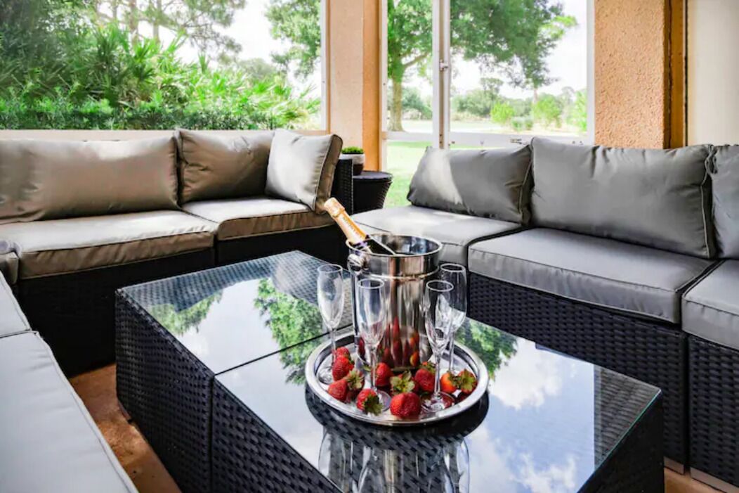 Un espace extérieur moderne, aménagé avec des sièges confortables, une table à plateau de verre, un seau à champagne et des verres, le tout entouré de canapés moelleux.