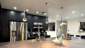 Une cuisine moderne dotée d’appareils électroménagers en acier inoxydable, de luminaires suspendus et d’un îlot central agrémenté de vases décoratifs.