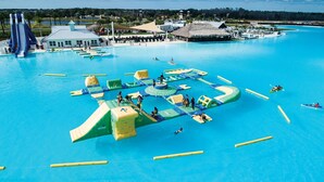 Vue aérienne d’un parc aquatique avec différentes structures de jeux, une grande piscine et une zone de plage avec des parasols.