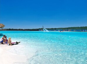 A beach with clear turquoise water, a thatched umbrella, and people relaxing on the sand.
