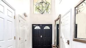 A hallway with two black doors, a large mirror, and a chandelier. - DisneyMansion by AmericanVacationLiving 11BR (Davenport)