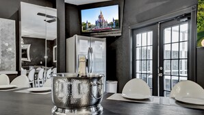 A modern kitchen with a large island, a built-in refrigerator, and a television displaying a castle. - DisneyMansion by AmericanVacationLiving 11BR (Davenport)