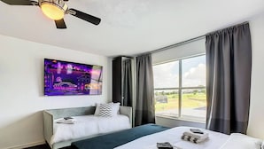 A hotel room with two beds, a ceiling fan, a large window with curtains, and a cityscape painting on the wall. - DisneyMansion by AmericanVacationLiving 11BR (Davenport)
