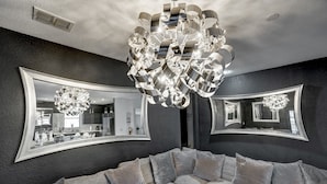 A modern living room with a large, curved mirror and a contemporary chandelier. - DisneyMansion by AmericanVacationLiving 11BR (Davenport)