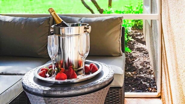 A champagne bottle in a metal bucket on a wicker table with strawberries.