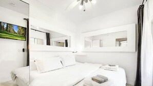 A modern hotel room with a large bed, two bedside tables, a ceiling fan, and a large mirror.