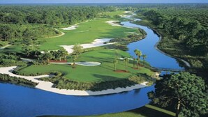A golf course with a water body, sand bunkers, and dense greenery.