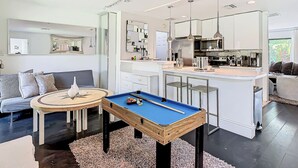 A modern living room with a pool table, a sofa, and a kitchen area with a dining table.