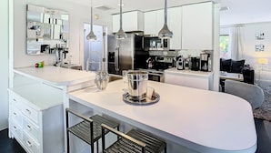 A modern kitchen with a central island, stainless steel appliances, pendant lighting, and a large mirror above the countertop.