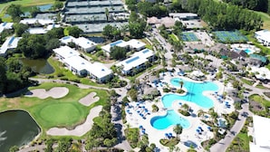 An aerial view of a resort with multiple buildings, a large swimming pool, and golf courses.