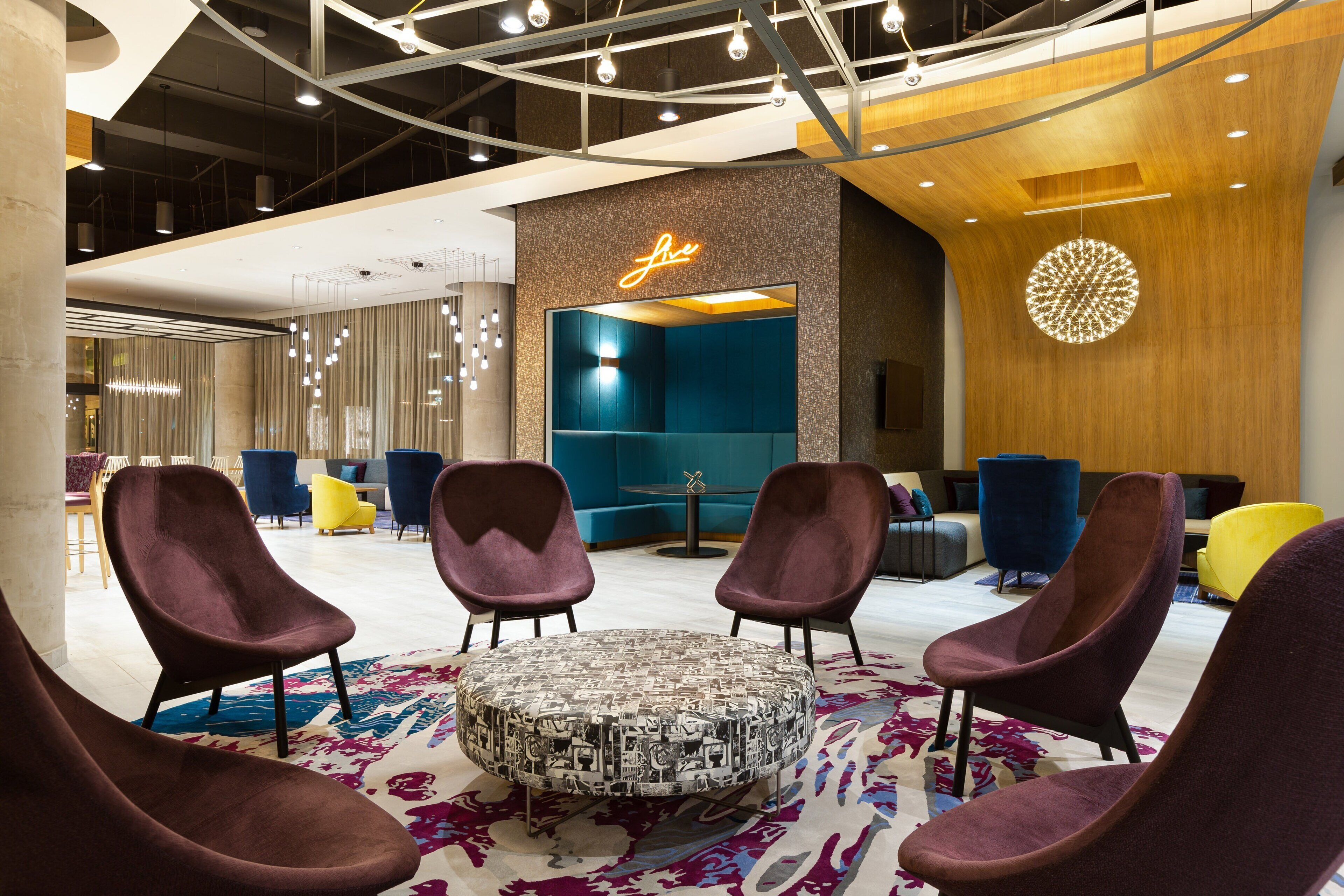A modern lobby with a round coffee table, purple chairs, and a neon sign.