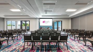 A conference room with rows of chairs, a projector screen, and a colorful carpet.