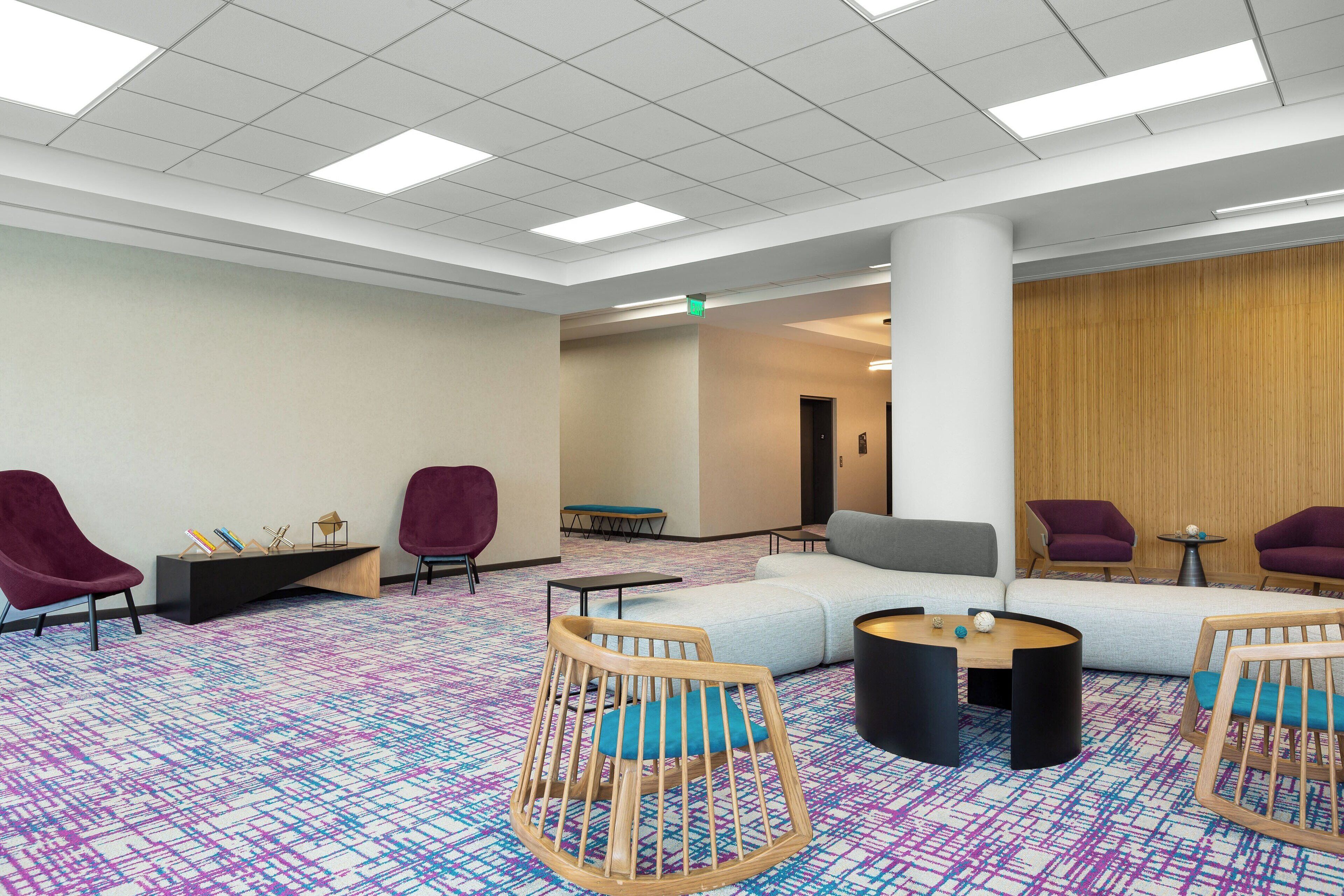 A spacious lobby with a colorful patterned carpet, a large sectional sofa, and multiple seating areas including wooden rocking chairs and purple armchairs.