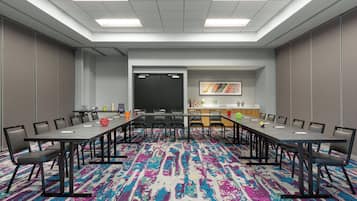 Un salón de conferencias con una larga mesa, sillas, una pantalla de proyector y una alfombra colorida.
