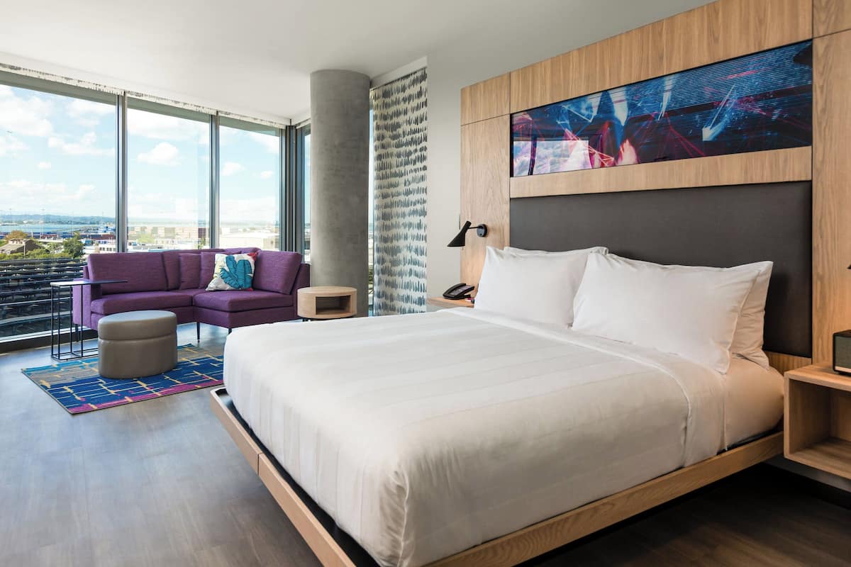 Habitación de hotel moderna con una cama grande, un sofá, una mesita y vistas a la ciudad.