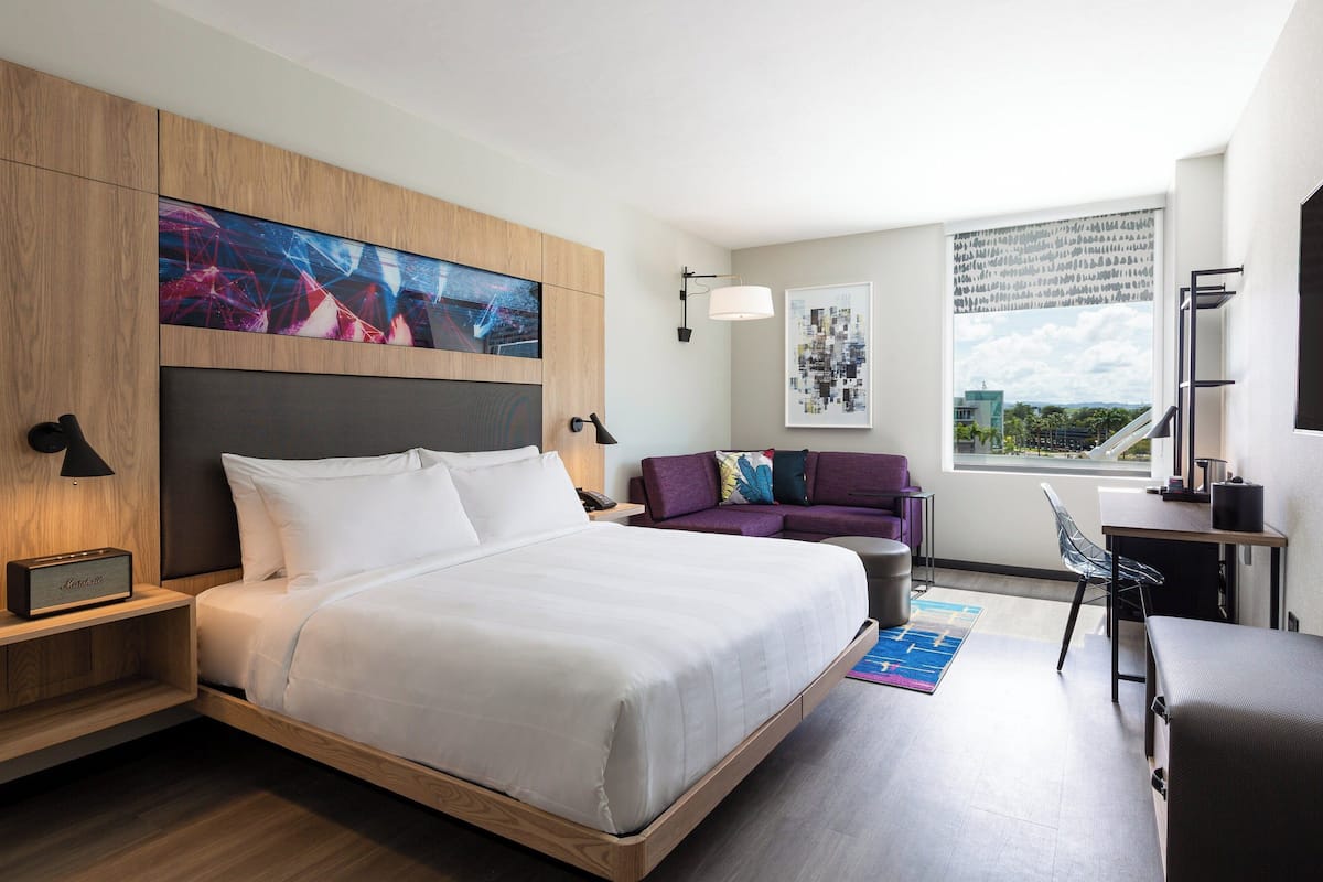 Una habitación de hotel moderna con una cama grande, un escritorio, una silla, un sofá y una ventana con vista a la ciudad.