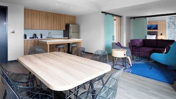 Une cuisine moderne avec des meubles en bois, un réfrigérateur en acier inoxydable et un coin bar. On y trouve une table à manger avec des chaises et un canapé dans l’espace salon.