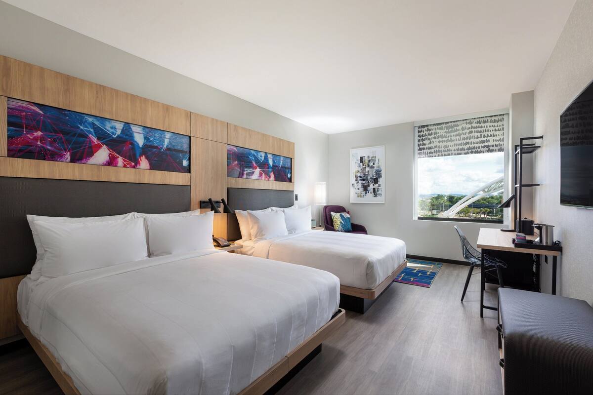 Una habitación de hotel con dos camas, un escritorio, una silla y obras de arte en las paredes.