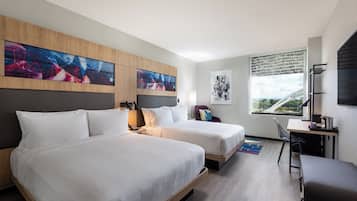 Een hotelkamer met twee bedden, een bureau, een stoel en kunstwerken aan de muur.