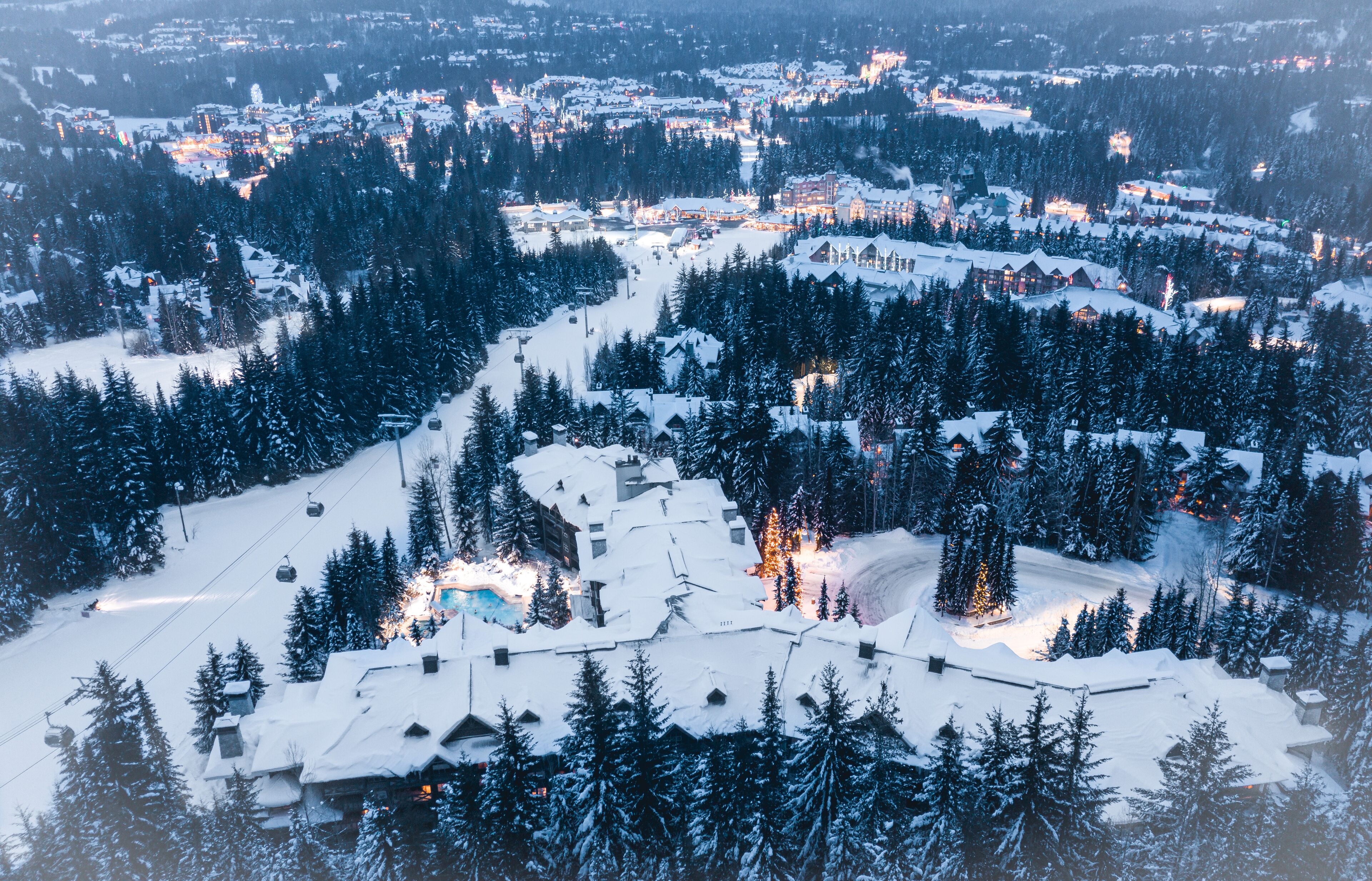 Et skisportssted dækket af sne med flere bygninger, stolelifter og en tæt skov.