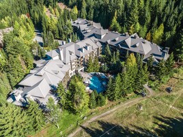 Vista aérea de un resort con varias construcciones, una piscina y bosque circundante.