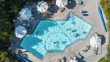 Vue aérienne d’un espace piscine comprenant plusieurs chaises longues, des parasols et quelques personnes qui se baignent.