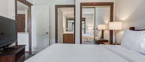 Habitación de hotel con una cama grande, televisión sobre un soporte de madera, armario y espejo en la pared.