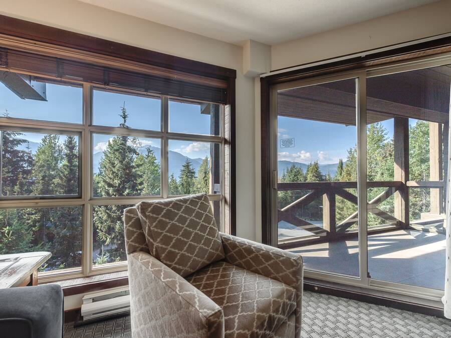 Una habitación con un ventanal amplio que ofrece vistas a una terraza de madera y montañas.