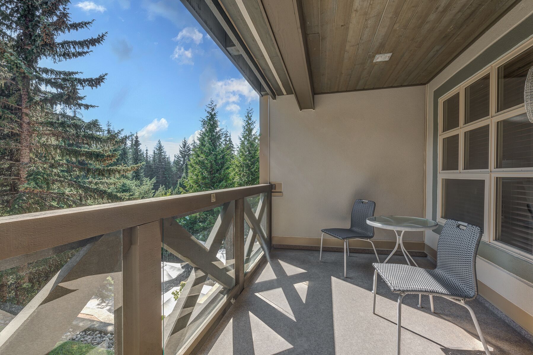 A balcony with a view of trees, a table, and two chairs.