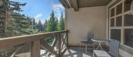 A balcony with a view of trees, a table, and two chairs.