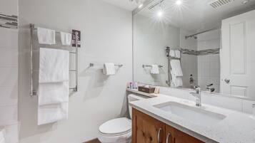 Un baño moderno con un inodoro blanco, un tocador de madera con un lavabo y un espejo grande.