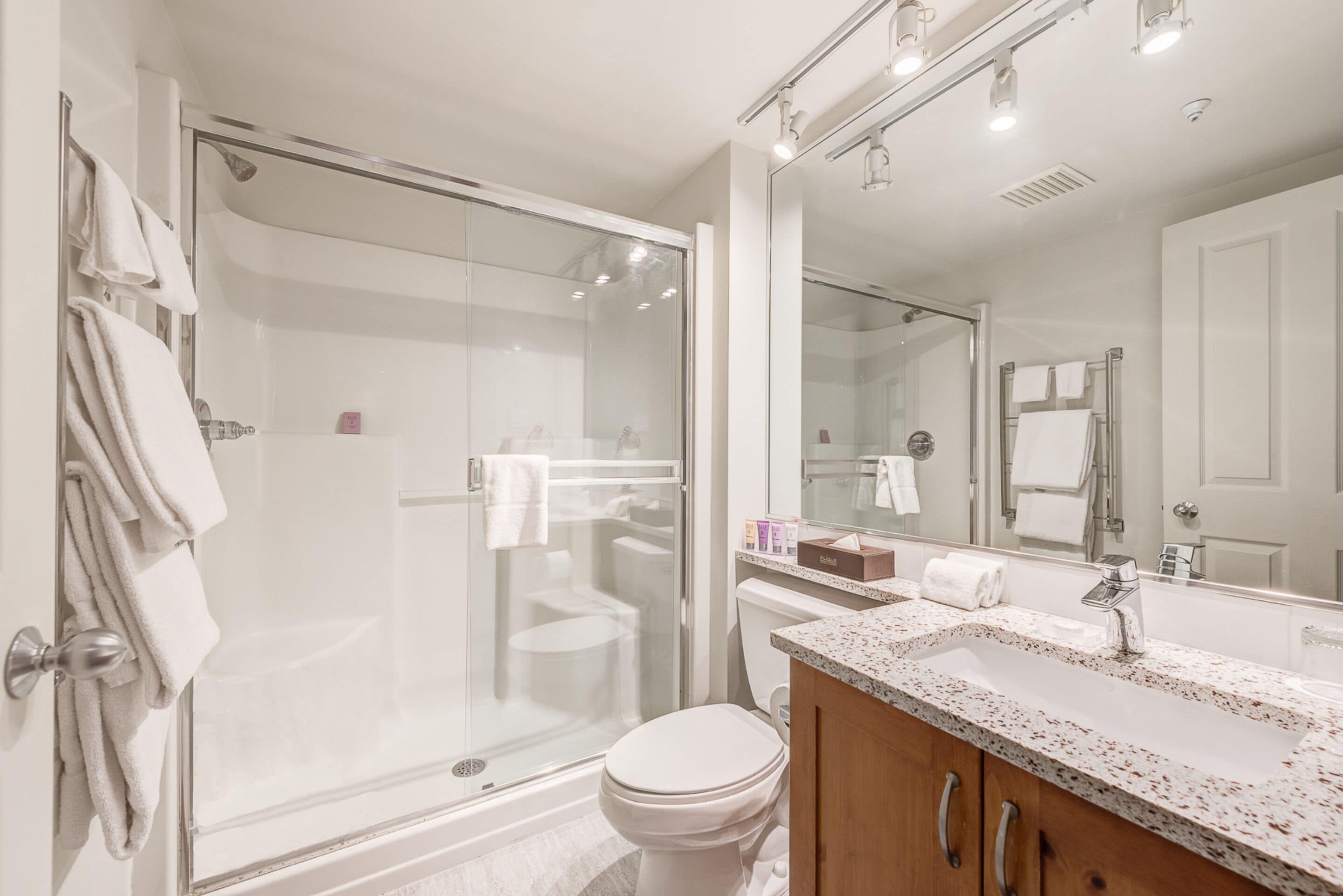 Un bagno moderno con cabina doccia in vetro, un water bianco, un lavandino con piano di appoggio maculato e uno specchio grande.
