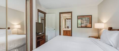 A hotel room with a large bed, a TV, a desk, and a mirror.