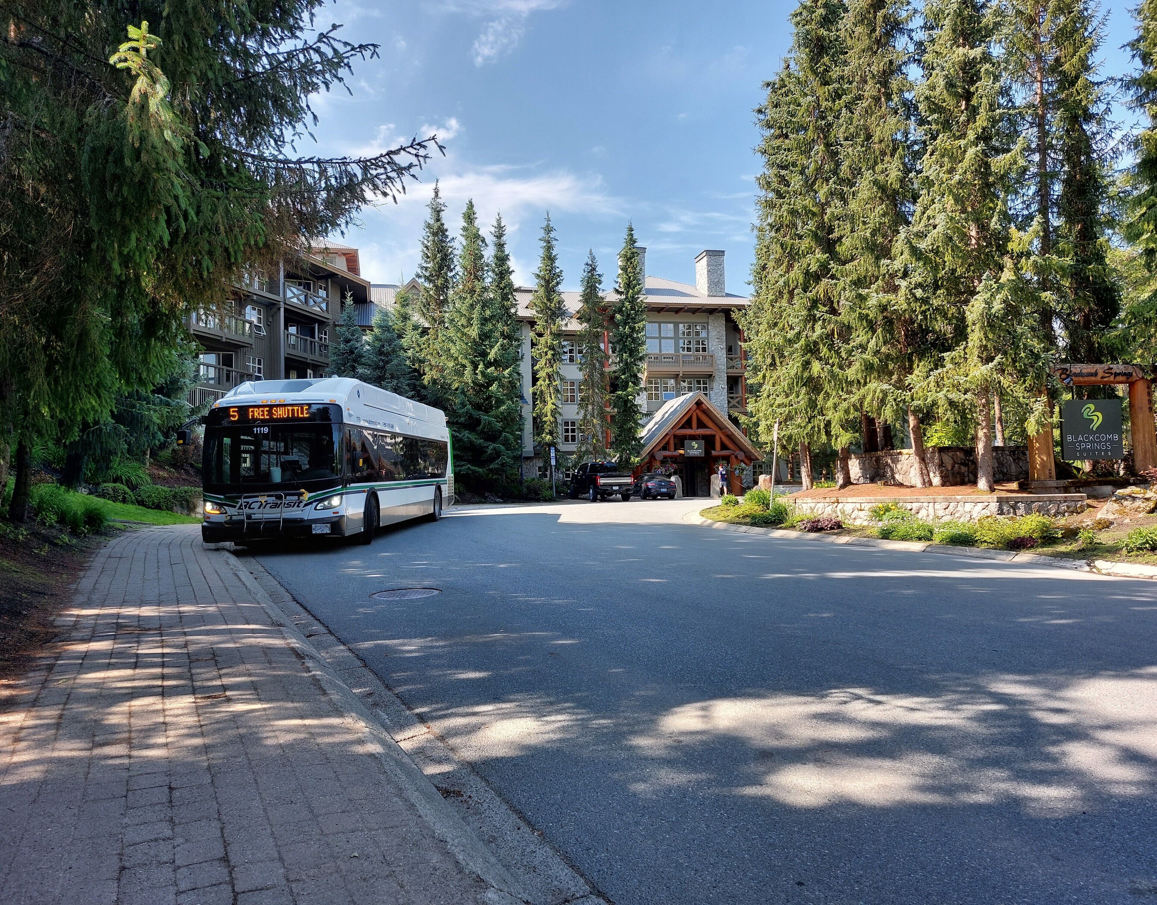 A bus labeled "Free Shuttle" approaching a lodge with a stone facade and a sign for "Blackcomb Springs Suites".