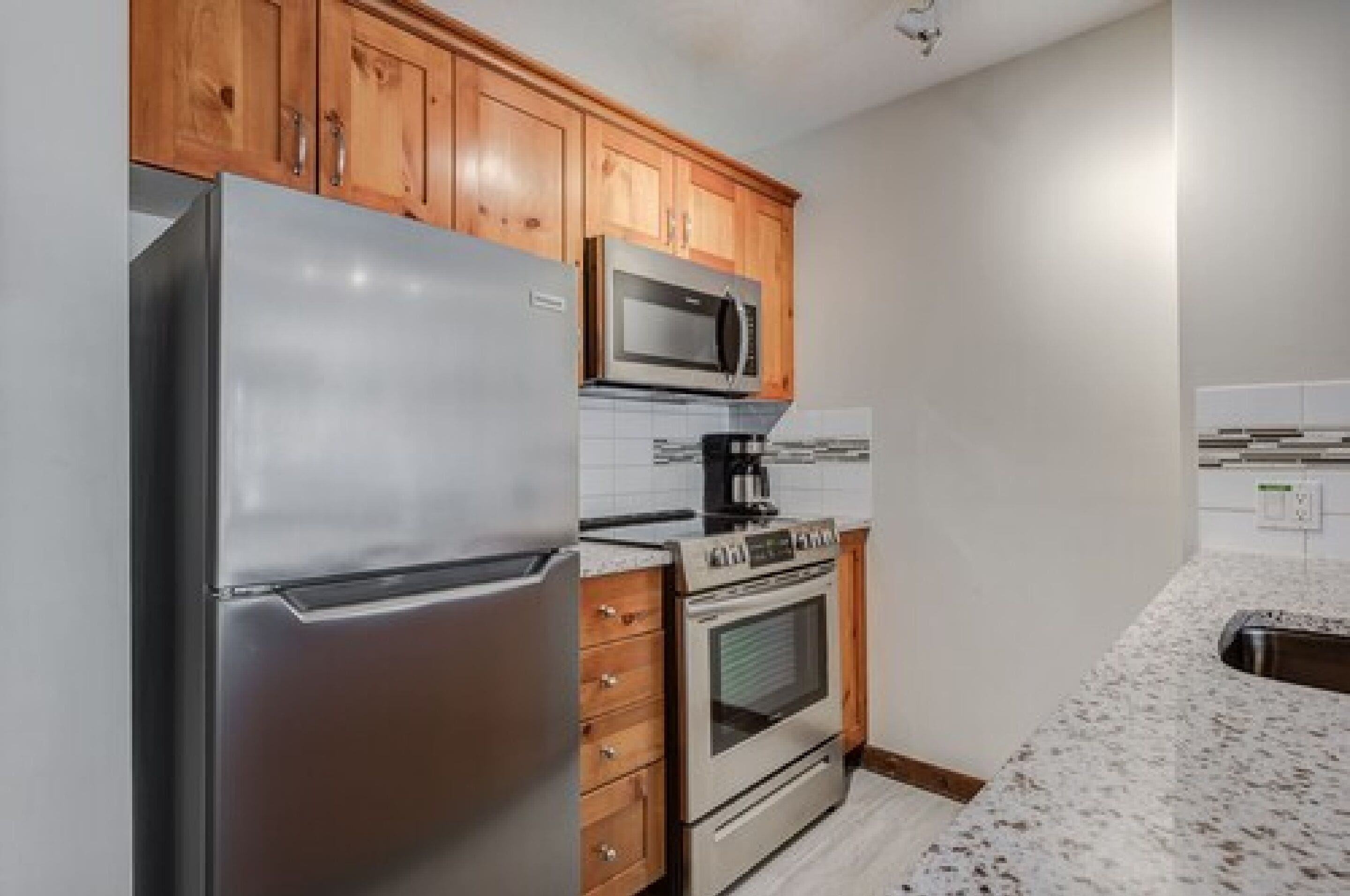 Una cocina con armarios de madera, un refrigerador de acero inoxidable, un microondas, un horno y un salpicadero de azulejos.