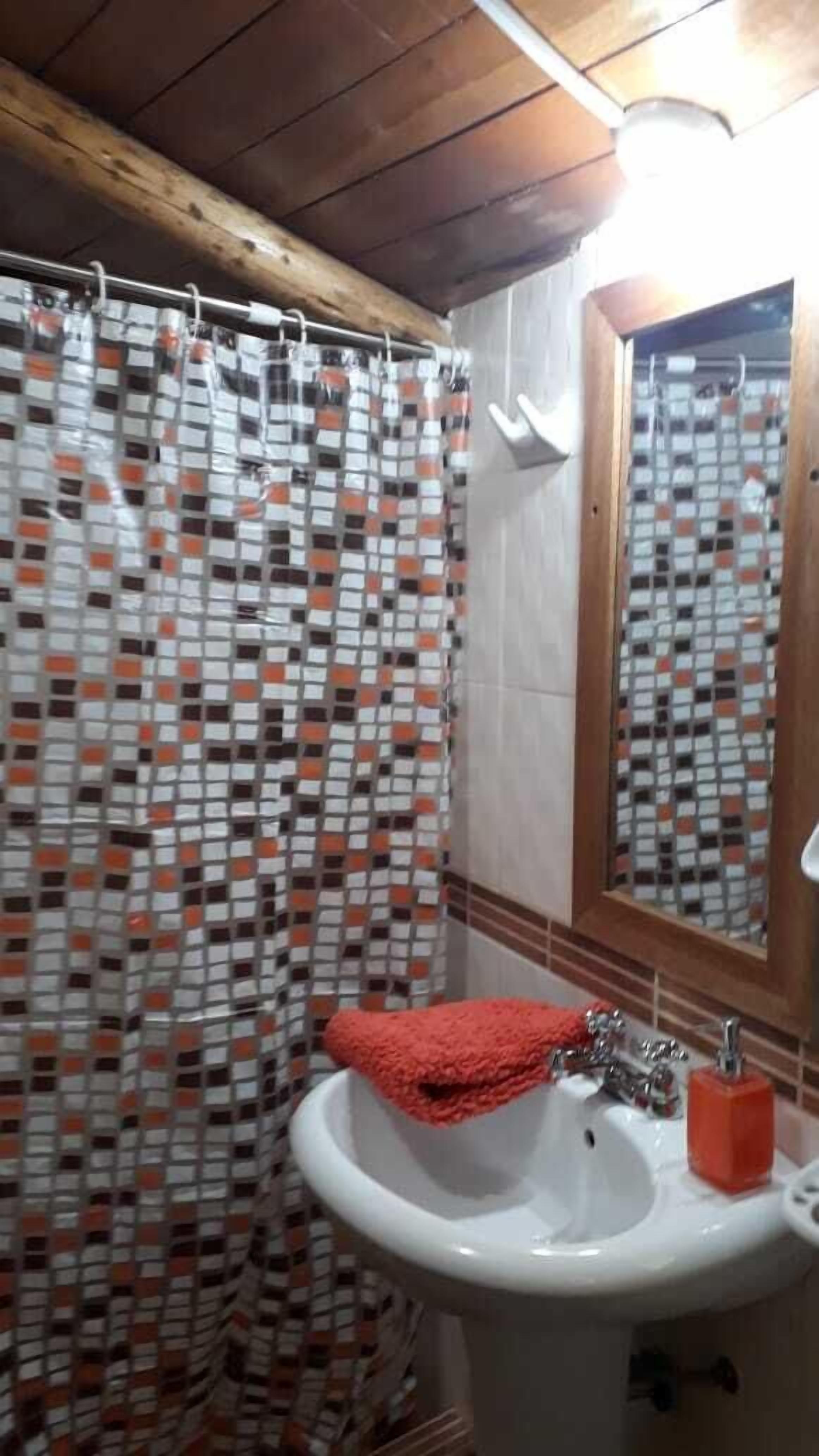 Un baño con cortina de ducha estampada, un lavamanos con una toalla roja y un espejo con marco de madera.