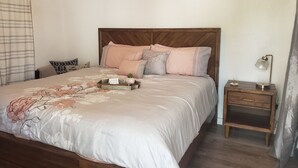 A neatly made bed with a floral bedspread, a wooden headboard, and a bedside table with a lamp. - Ocean Park 2nd Floor King-Size Mini-Studio (Santurce)