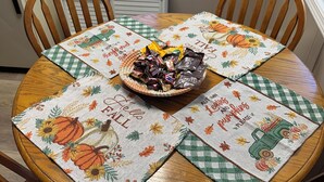 A round wooden dining table with a floral table runner and a bowl of assorted snacks.