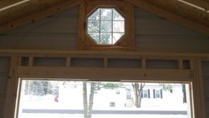 A wooden attic with exposed beams, a hexagonal skylight, and a large window at the bottom.