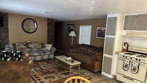 A cozy living room with a plaid sofa, a brown couch, a wooden chair, a coffee table, and a vintage stove.