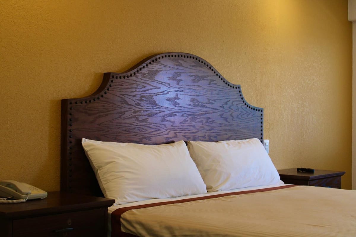 A bed with a wooden headboard, two pillows, a bedside table with a phone, and a nightstand.