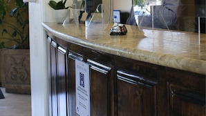 A reception desk with a marble top, a potted orchid, a framed photo, and a sign indicating a business center. - Estancia Inn (Tecate)