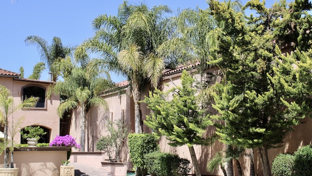 A building with a stucco exterior, a tiled roof, and a large tree in front. - Estancia Inn (Tecate)