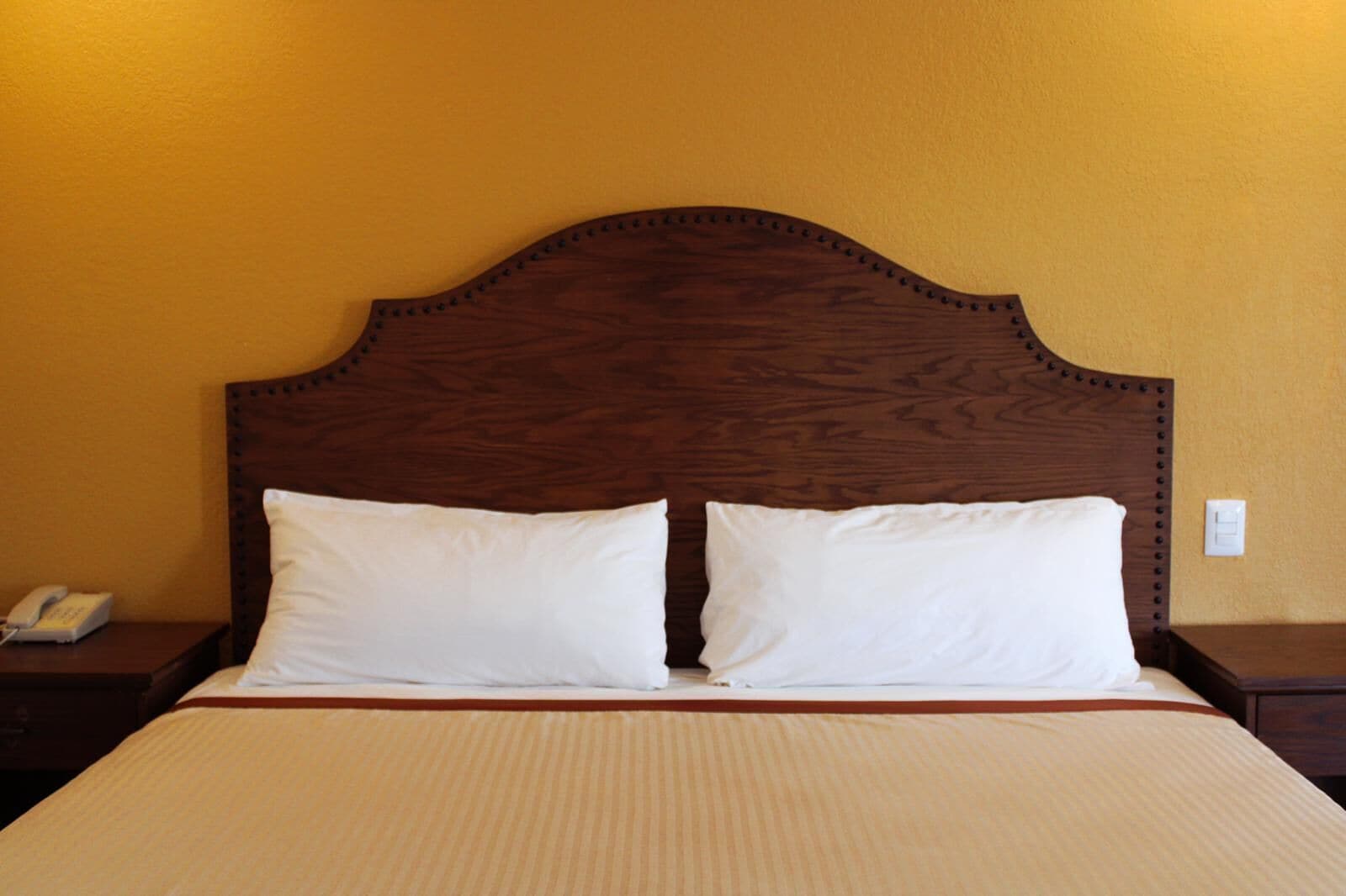 Una cama con cabecera de madera, dos almohadas blancas y una colcha color beige.