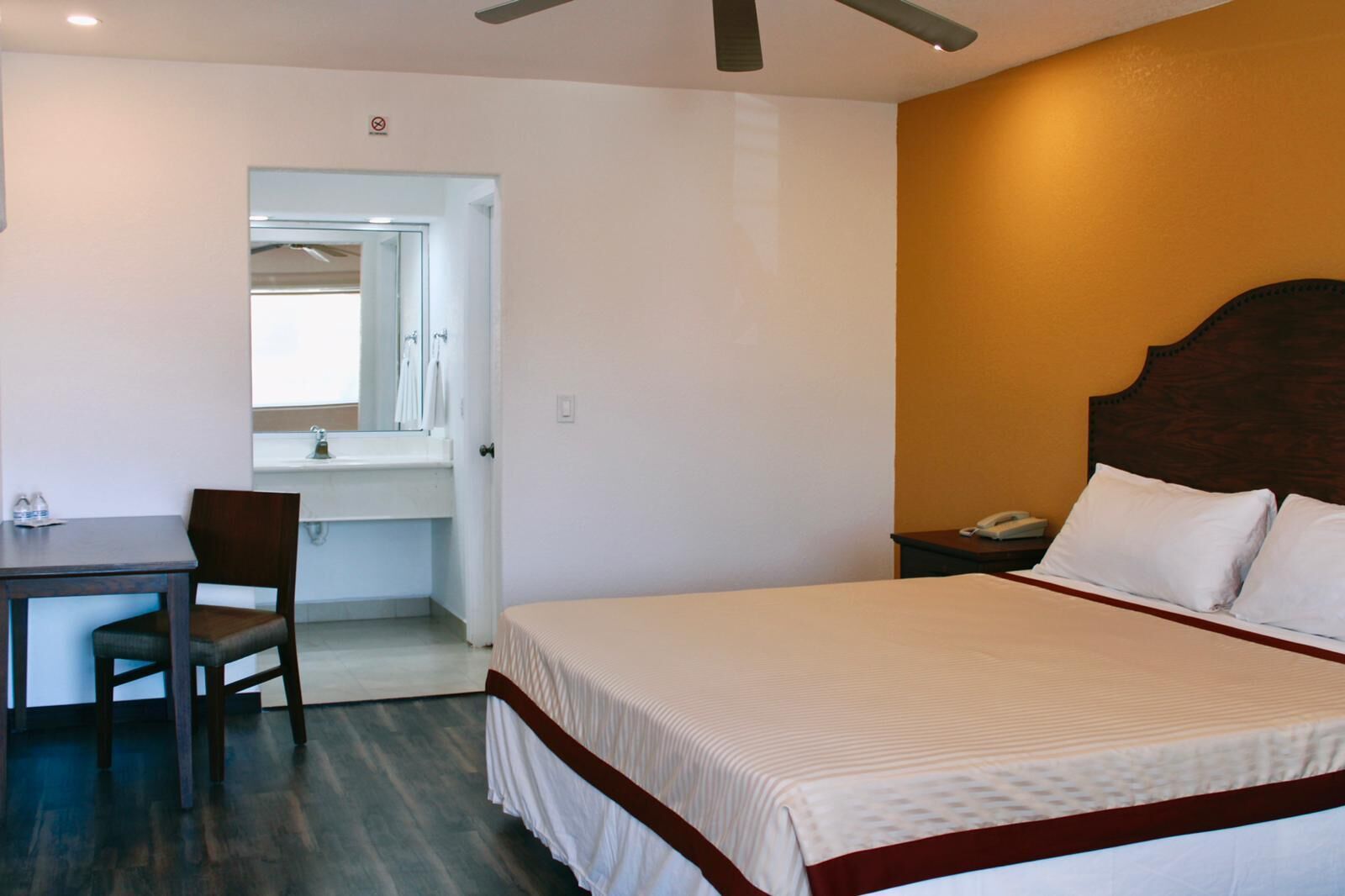 A hotel room with a bed, a desk, a chair, a nightstand, and a bathroom visible through an open door.